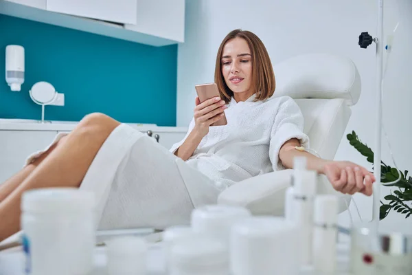 Happy smiling woman sitting in medicine armchair during medical procedure in beauty center