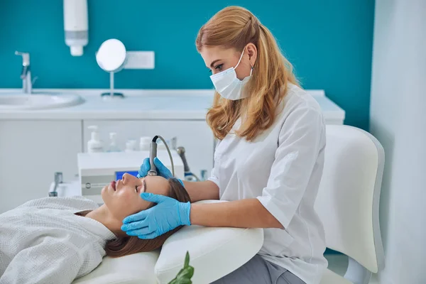 Beautiful elegant doctor in white uniform doing skin care for pretty lady in beauty clinic — Foto Stock