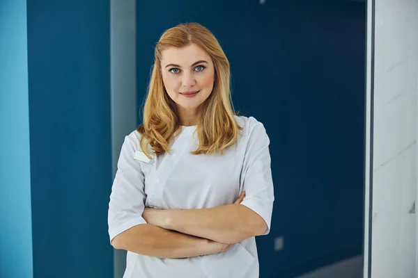 Adult Caucasian blonde beautician standing on blue background in medicine center — ストック写真