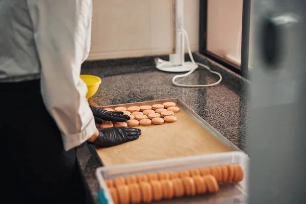 Qualified pastry cook organising crisp macarons on a baking tray — Stok fotoğraf