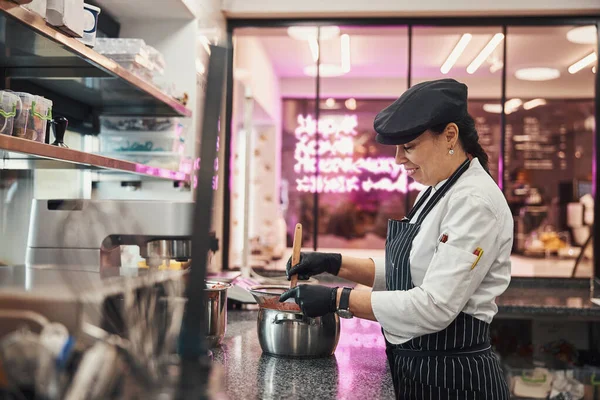 Pleased pastry chef stirring her concoction in metal pan — Stok fotoğraf