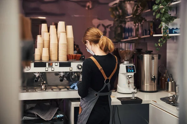 Focused woman in barista uniform making coffee for customers — Photo