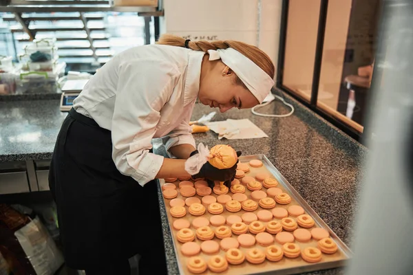 Focused pastry chef putting icing on custom-made macarons — Stockfoto