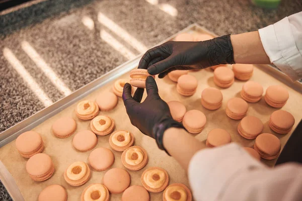 Skillfull confectioner in black gloves creating hand-made macarons — Stok fotoğraf