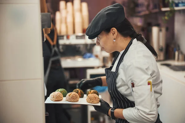 Kvalificerad sötsaker som tar nybakade dessertscones ur ugnen — Stockfoto