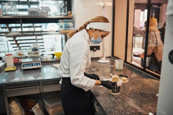 Mulher responsável em uniforme de chef e máscara fazendo sobremesas — Fotografia de Stock