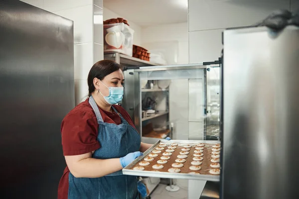 Maskeli ve önlüklü esmer kadın badem kurabiyesi pişirmeye hazırlanıyor. — Stok fotoğraf