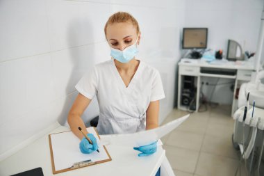 Kadın diş hekimi röntgen sonuçlarını kağıda kopyalıyor.