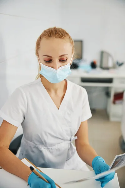 Schreibender Stomatologe mit Röntgenbild am Tisch — Stockfoto