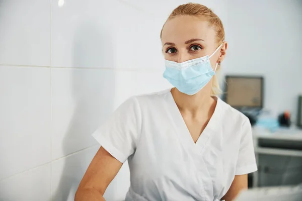 Zahnarzthelferin sieht Kamera, während sie in Maske sitzt — Stockfoto