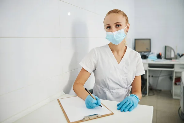 Serious dentist posing with pen and notepad to camera