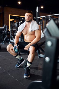 Spor salonunda tişörtsüz poz veren kaslı bir adam.