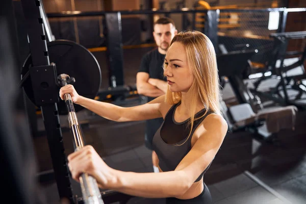 Dama trabajadora haciendo ejercicio en el gimnasio con la ayuda del entrenador — Foto de Stock