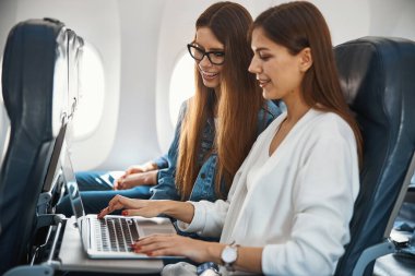 Uçakta dizüstü bilgisayar kullanan iki güzel bayan.