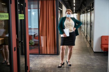 Kendine güvenen kişisel asistan ofis koridorunda kameraya bakıyor.