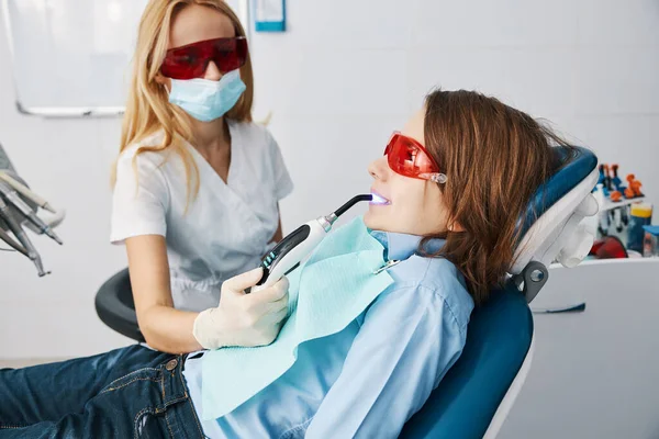 Female dentist setting sealants on teeth with LED curing lights — Stock Photo, Image