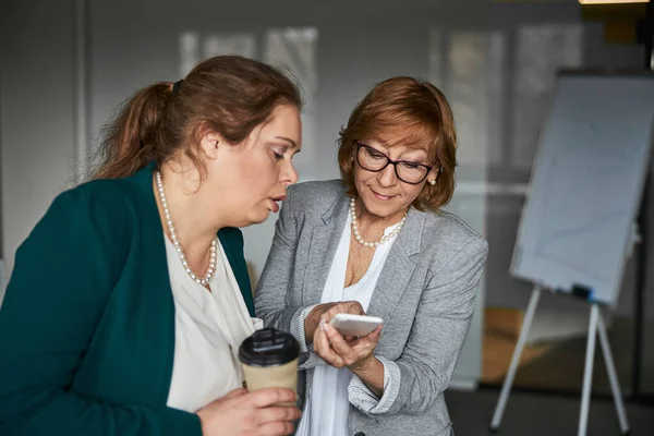 Chefin bedient ihr Smartphone, während interessierte Frau hineinguckt — Stockfoto