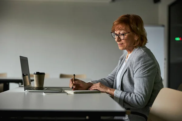 Reif weiblich im büro schreiben im notizblock — Stockfoto