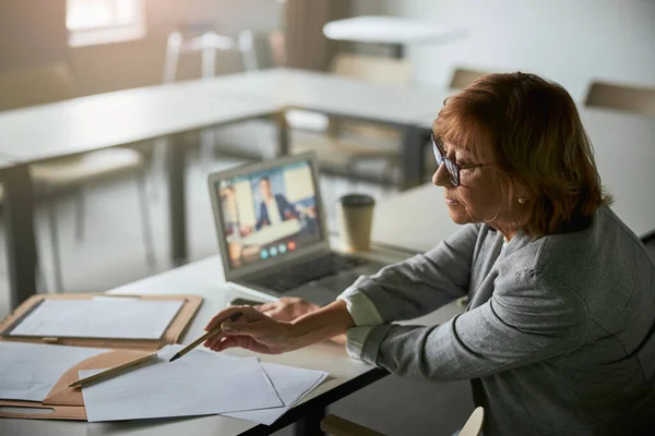 Aufmerksame Frau prüft Informationen mit Dokumenten auf dem Tisch — Stockfoto