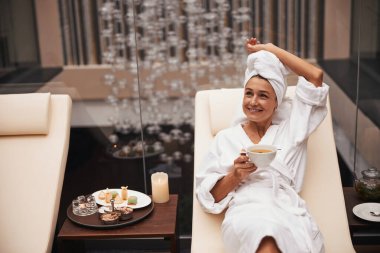 Başında havluyla, sağlık merkezinde bitki çayıyla rahatlayan çok çekici bir kadın.