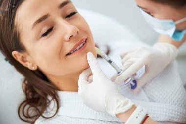 Kırışıklık önleyici iğne yaptıran mutlu, siyah saçlı kadın.