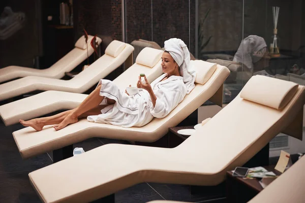 Encantadora mujer blanca joven positiva con toalla en la cabeza relajante y descansando en el centro de bienestar —  Fotos de Stock