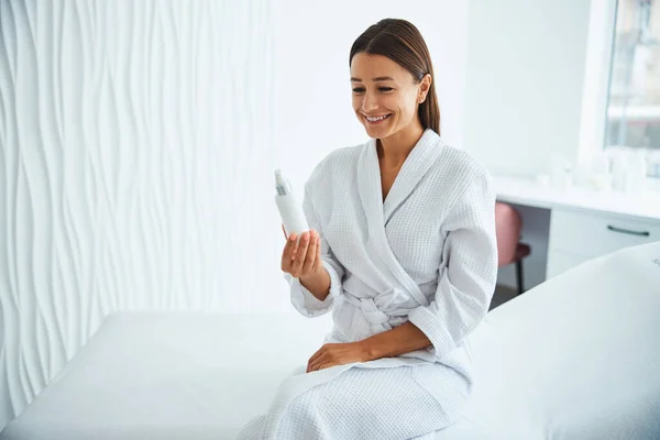 Woman in a bathrobe looking at a cosmetic product — Stock Photo, Image