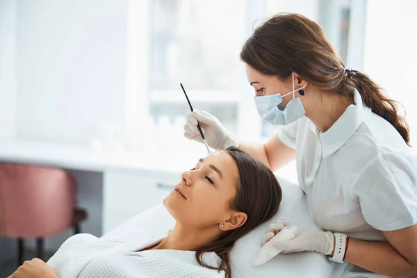 Dermatólogo aplicando una mascarilla facial a la piel del paciente —  Fotos de Stock