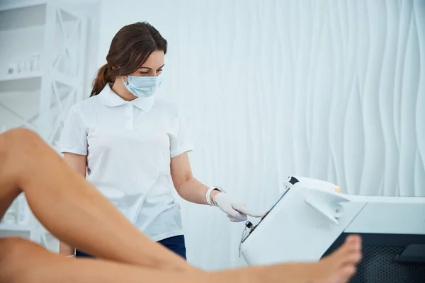 Allvarlig kosmetolog som justerar behandlingsparametrarna på en lasermaskin — Stockfoto
