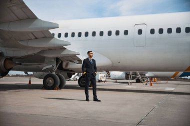 Erkek pilot uçağın önünde dinleniyor.