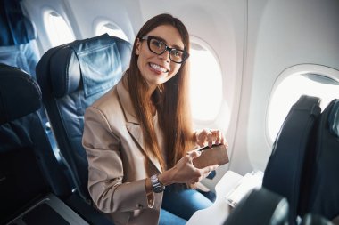 Kutu tutarken uçak penceresinin yanında oturan mutlu kadın.