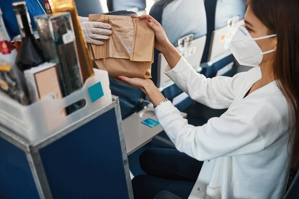 Kvinna i mask accepterar papperspåse från flygvärdinna händer — Stockfoto