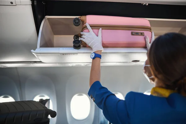 Flygarbetare som gömmer handbagage med hjul i bagageutrymmet — Stockfoto