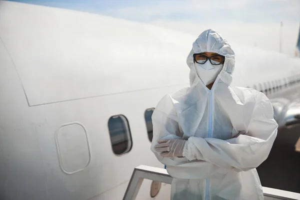 One woman in hooded protective clothes crossing arms near airplane