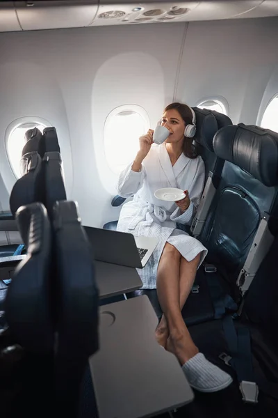 Žena v županu a sluchátka pití kávy v letadle — Stock fotografie