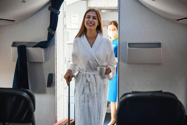 Расслабленная женщина входит в каюту самолета в халате с кофе — стоковое фото