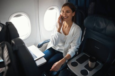 Uçaktayken telefonda konuşan neşeli bir kadın.