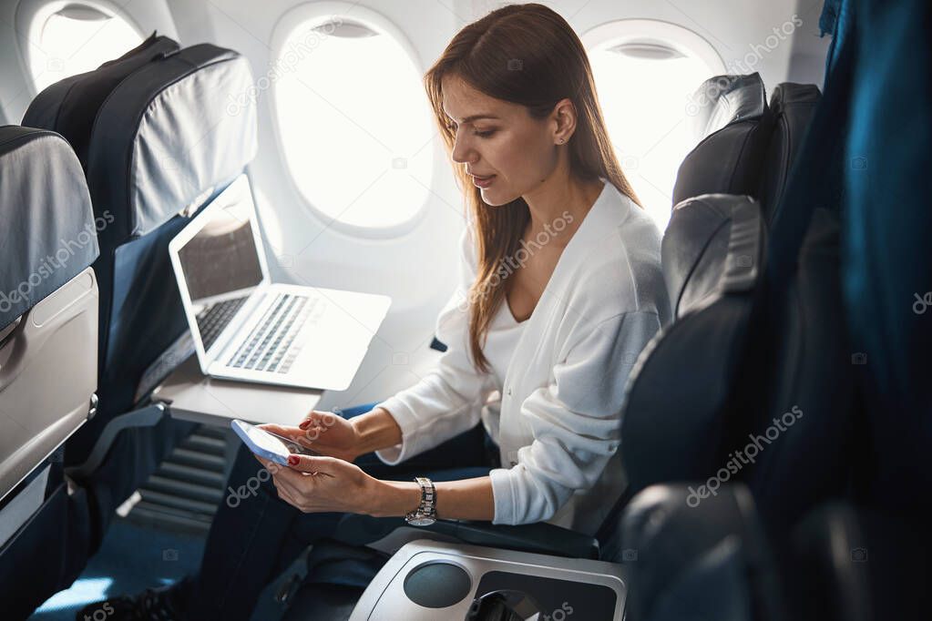 Calm young lady with two modern gadgets in the plane