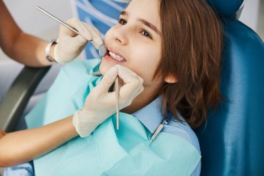 Diş hekimi çocuğun ağzına ayna ve sondayla uzanıyor.