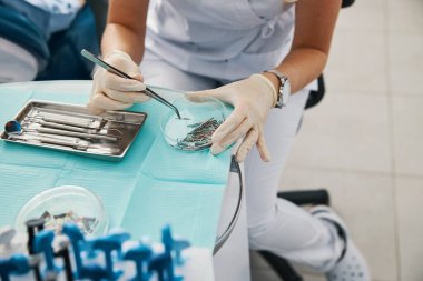 Diş hekimi tepsiden pamuklu forseps alıyor.