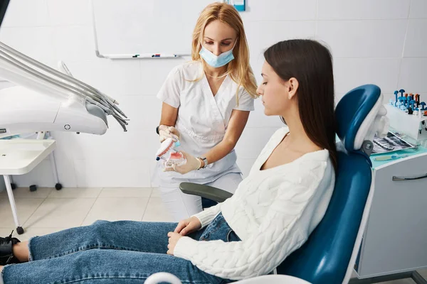Жінка-стоматолог рухає зубну щітку на верхньому ряду зубів маскування — стокове фото