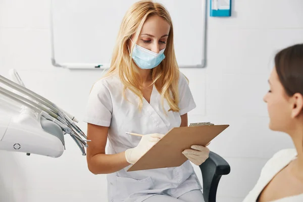 Zahnmediziner macht sich Notizen in Papier auf Klemmbrett — Stockfoto
