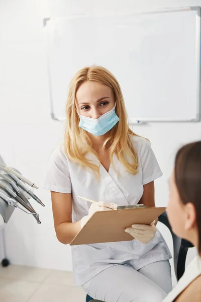 Betrokken stomatoloog op zoek naar vrouw tijdens het schrijven van informatie — Stockfoto