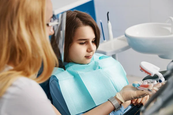 Cirurgião dentário ensinando menor como escovar os dentes no modelo — Fotografia de Stock