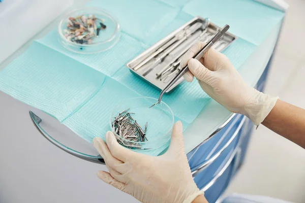 Dental burs lying in glass bowl while dentist taking one — Stock Photo, Image