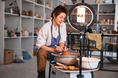 Toprak malzemelerini çömlek aletleriyle budamaya çalışan konsantre bir kadın.