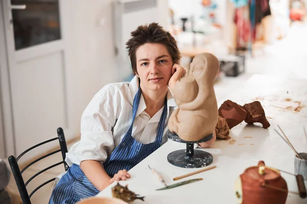 Mujer ceramista posando para cámara cerca de modelo de arcilla —  Fotos de Stock