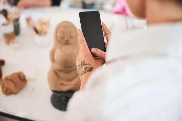 Mobiele telefoon in handen van persoon in de buurt van aardewerk standbeeld — Stockfoto