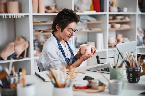 Potter showing ceramic cup to laptop screen — Stock Photo, Image