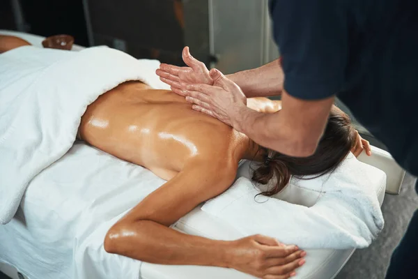 Niet herkende mooie dame liggend op massage bed terwijl onherkende therapeut het maken van terug massage in wellness centrum — Stockfoto